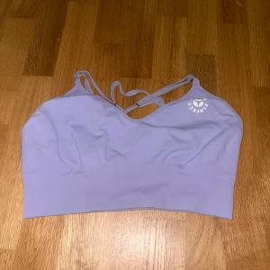 Ljuslila sportig linnetopp från ICIW - Supersnygg ljuslila linnetopp från ICIW med tunna korsade axelband i ryggen och diskret logga framtill. Perfekt för träning eller chill dagar. Mjuk och stretchig syntetblandning som sitter skönt och följer kroppen. Storlek S passar M 