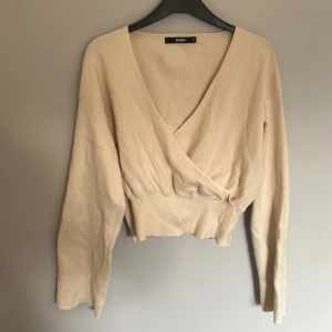 Krämvit omlottstickad tröja BikBok - Superfin krämvit stickad tröja från BikBok med omlott och v-ringad hals. Modellen är croppad med bred resår i midjan och har långa ärmar. Perfekt för lager-på-lager och passar till både jeans och kjol. Lite hundhår på tröjan samt lite fläckigt här och var vilket gör priset lite lägre.