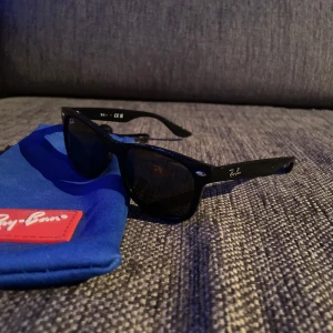 Svarta Wayfarer Ray-Ban - Klassiska svarta Wayfarer solglasögon från Ray-Ban. Dem passar 8-13 åringar och Kommer med blå Ray-Ban-fodral. Perfekta för att lyfta din stil i sommar.