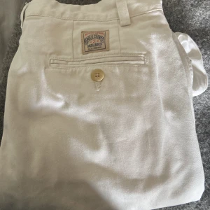 Vita chinos från Polo Ralph Lauren - Snygga vita chinos från Polo Ralph Lauren med klassisk passform och raka ben. Byxorna har fickor fram och bak, knappstängning och bälteshällor. Tillverkade i bomull för en skön och stilren känsla. Perfekta för en clean och fräsch look. Storlek: 14/164, oanvända, kan tänka mig byta mot vita chinos/jeans 28/29 i midjan och runt 30-32 i längd! Kontakta vid frågor!