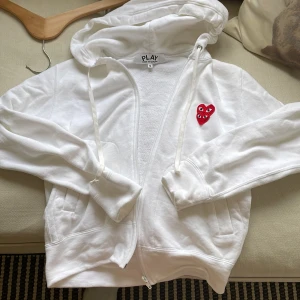 Vit hoodie Comme des Garçons Play S - Vit hoodie från Comme des Garçons Play med dragkedja och huva. På bröstet sitter två röda hjärtan med ögon, en ikonisk detalj från märke. Perfect nu på sommaren ☀️nypris 3000kr mitt pris 450kr. Storlek S men passar mer som en xs eller xxs eftersom den sitter lite tajt på mig som är 164cm lång. Fråga om funderingar. Inget tecken på andvändning