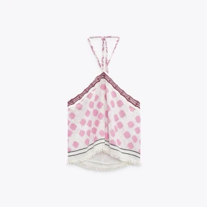 Prickig halterneck linnetopp - Supersöt linnetopp med rosa prickar på vit botten, halterneck med knyt i nacken och spetsdetalj upptill. Toppen har fransig kant nertill och är perfekt för varma dagar. Ingår ej frakt, tappat lite av spetsdetaljen 