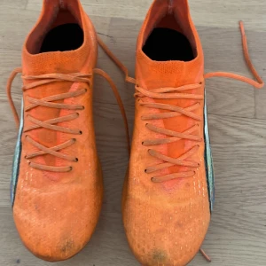 Puma Ultra orange fotbollsskor ganska använda med bra skick  - Säljer ett par grymma Puma Ultra fotbollsskor i en riktigt snygg orange färg med svarta och vita detaljer på sidan. Skorna har snörning och är tillverkade i lätt syntetmaterial för maxad speed på planen. Perfekta för dig som vill sticka ut på matchen!
