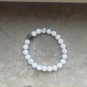 Vitt pärlarmband med marmormönster - Stilrent armband med runda vita pärlor och gråa marmordetaljer. En av pärlorna är svart och fyrkantig vilket ger en cool kontrast. Perfekt accessoar för att lyfta din outfit med en minimalistisk touch.