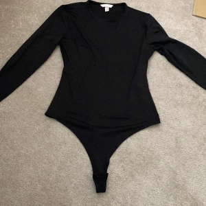 Svart långärmad bodysuit H&M - En svart, långärmad bodysuit från H&M med rund halsringning. Tight passform och klassisk design som sitter snyggt till både jeans och kjol. Gjord i mjukt och stretchigt material för en bekväm känsla hela dagen.