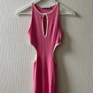 Rosa ribbad cut out-klänning Bershka - Rosa ribbad klänning från Bershka med vita kanter, cut out-detaljer i midjan och en snygg öppning framtill vid halsen. Klänningen har en tight passform och går nedanför knäna. Älskar men kommer tyvärr inte till användning tillräckligt ofta, använd 2 gånger.