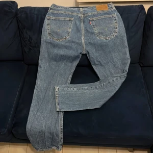 Levi's 501 klassiska blå straight jeans - Klassiska Levi's 501 jeans i ljusblå tvätt med raka ben och normal passform. Jeansen har fem fickor, knappgylf och den ikoniska läderpatchen bak i midjan. Tillverkade i slitstarkt bomullsjeans med snygga kontrastsömmar och röd Levi's-tagg på bakfickan. Storlek: Midja: 34 Längd: 32. Original pris: 800 - 1000kr