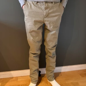 Beige chinos från Jack & Jones - Snygga beige chinos från Jack & Jones med klassisk rak passform. Byxorna har bälteshällor, sidofickor och två bakfickor. Tillverkade i mjuk bomull som känns skön mot huden. Perfekta för en clean och stilren look. Storlek W29 L32