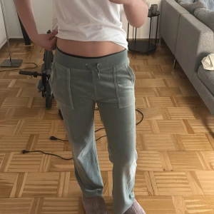 Gröna mjukisbyxor i velour med snörning - Snygga ljusgröna mjukisbyxor från Juicy Couture i mjuk velour. Byxorna har snörning i midjan, raka ben och fickor både fram och bak, Bakfickorna har knappdetaljer. Broderad JC-logga på ena fickan. Perfekta för en chill och trendig look. Lite slitningar vid snörena men inget man direkt tänker på. Orginal pris är 1200kr men jag säljer för 860kr. Säljer pga att dem är lite för korta för mig och att dem inte kommer till användning längre. Jag är 158.