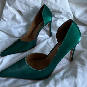 Gröna pumps med spetsig tå - Snygga pumps i smaragdgrönt med spetsig tå och hög klack. Skorna har en elegant siluett och är tillverkade i ett glansigt material som ger en lyxig känsla. Perfekta för att lyfta vilken outfit som helst.