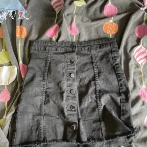 Svart jeanskjol med knappar, g perfect jeans - Svart kort jeanskjol från g perfect jeans i storlek 38. Kjolen har raka sömmar, knappar framtill och rå kant nertill för en cool look. Perfekt till sneakers eller boots för en avslappnad stil.