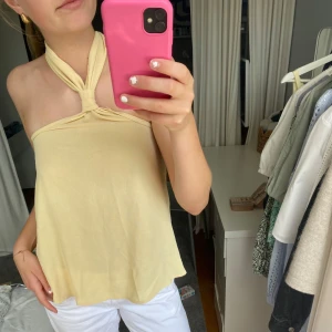 Ljusgul halterneck linnetopp - Supersöt ljusgul halterneck topp med knyt runt nacken och öppen rygg. Den är aldrig använd så jättebra skick! Passar både till vardagen men också på fest. 