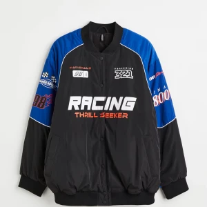 Racing bomberjacka svart/blå - Snygg bomberjacka med racing-inspirerade tryck och brodyr. Jackan är svart med blå ärmar och detaljer i vitt och rött. Ribbstickade muddar och krage, tryckknappar framtill och coola patches på bröst och ärmar. Perfekt för dig som gillar streetstyle och sportig vibe. Oversized i storleken så passar bra på M/L.