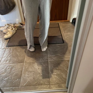 Grå mjukisbyxor med slits nertill - Säljer ett par ljusgrå mjukisbyxor i mjukt material. Byxorna har en loose passform och är raka i modellen med slits nertill vid bensluten. Perfekta för chill dagar hemma eller när du vill vara bekväm men ändå se snygg ut.