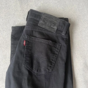 Svarta Levi's 511 jeans - Svarta jeans från Levi's modell 511 med klassisk femficksdesign och röd Levi's-tag på bakfickan. Jeansen har en smal passform och är tillverkade i mjukt jeanstyg med dragkedja framtill. Perfekta för en clean och stilren look. W 28/L32