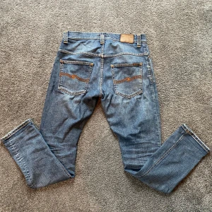 Nudie Jeans Thin Finn blå jeans W30 L32 - Säljer ett par blå Nudie Jeans Thin Finn i modellen skinny. Jeansen har klassiska bakfickor med orange brodyr och slitningar vid knäna. Tillverkade i 98% ekologisk bomull och 2% elastan för extra stretch. Perfekta för dig som gillar en smal passform.
