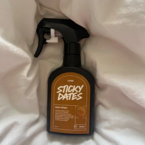 OANVÄND Lush Sticky Dates Body Spray 200ml - Lush Sticky Dates Body Spray i svart plastflaska med spraymunstycke. Doften är en limited edition och har en varm, söt och krämig ton av dadlar, vanilj och sandelträ. Flaskan rymmer 200 ml och har en brun etikett med vit text på framsidan.
