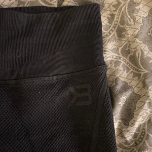 Svarta seamless tights från Better Bodies - Säljer ett par svarta seamless tights från Better Bodies med hög midja och diskret mönstrad struktur. Tightsen har tight passform och är perfekta för träning. Logga på linningen och sidan av benet. Använd väldigt få gånger, ny pris 699kr💛