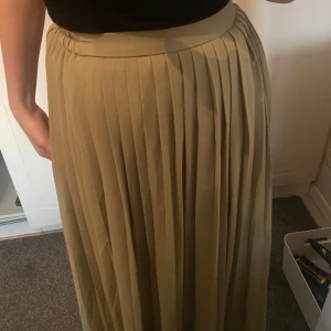 grön  plisserad långkjol - Säljer en beige plisserad långkjol med hög midja. Kjolen har ett snyggt fall och bred linning som ger en stilren look. Perfekt att matcha med en enkel topp för en trendig outfit.