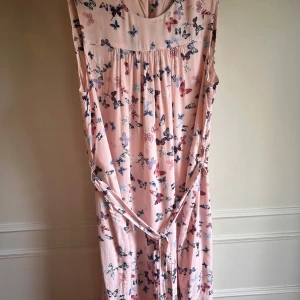 Rosa klänning med fjärilsmönster från Esprit - Charmig rosa klänning från Esprit med ett vackert fjärilsmönster i olika färger. Klänningen har en rund hals och är ärmlös, vilket gör den perfekt för varma dagar. Tillverkad i ett mjukt och bekvämt viskosmaterial.