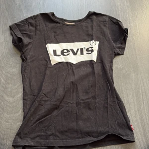 Svart t-shirt från Levi's - Säljer en klassisk svart t-shirt från Levi's med deras ikoniska logga i vitt på bröstet. T-shirten är kortärmad och gjord i mjuk bomull. Osäker på storlek men runt stl 158. Väl använd men ingenting som syns 
