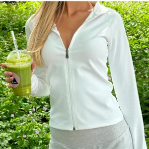 Vit träningskofta  - Säljer en stilren vit jacka från Nelly med dragkedja framtill. 