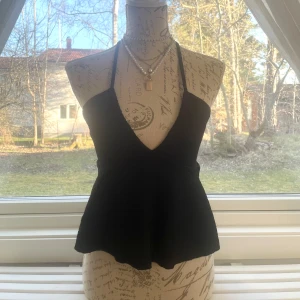 Svart halterneck linnetopp - Säljer en svart halterneck linnetopp med v-ringning och knyt i nacken. Toppen har en lätt utsvängd nederdel och är tillverkad i ett strukturerat, vågigt tyg. Passar storlek XS-S.