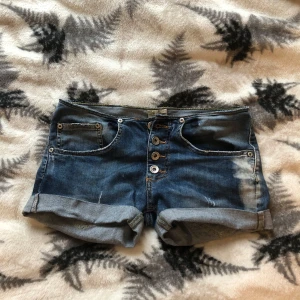 Jeansshorts med knappar - Snygga jeansshorts med upprullade ben och knappar framtill. Perfekta för en avslappnad sommarlook. De har fickor både fram och bak, med en liten hjärtdetalj på bakfickan. Skulle säga storlek Xs-S eftersom jag har klippt de lite för att de skulle bli mer lågmidjade😊