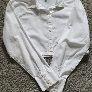 Vit croppad skjorta från Divided H&M - Säljer en vit croppad skjorta från Divided H&M. Skjortan har klassisk krage, långa ärmar och knäppning framtill. Perfekt för en stilren och trendig look. Passar dig som gillar enkla och snygga basplagg.