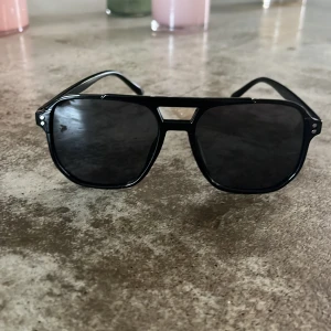 Svarta pilotbågar solglasögon - Snygga svarta solglasögon med pilotbågar och mörka linser. Ramen är i plast och har en klassisk, lite oversized form med markerad näsbrygga. Perfekt accessoar för att lyfta din stil. Kan gå ner i pris vid snabb affär