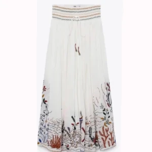 Vit långkjol med broderi från Zara - Superfin vit långkjol från Zara med färgglada broderade detaljer nertill och vågig mönsterkant i midjan. Kjolen har knytband i midjan och ett luftigt, flowy tyg som passar perfekt till varmare dagar.