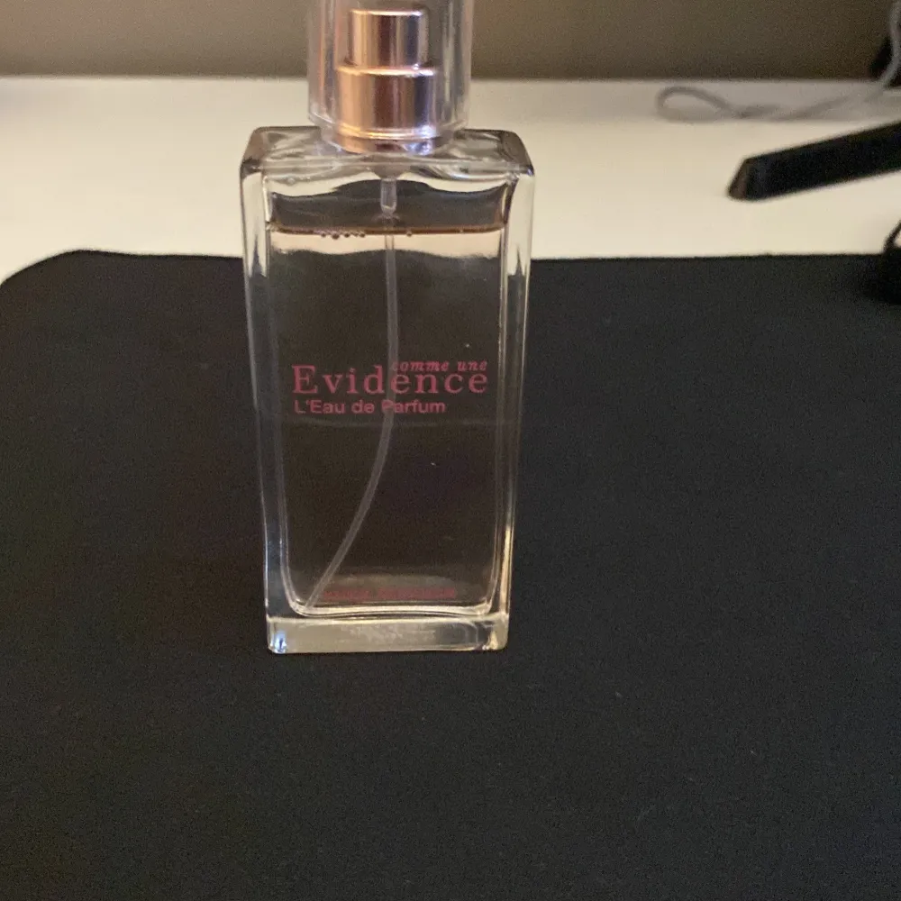 En elegant parfymflaska i genomskinligt glas med rosa text och silvrig spraykork. Doften är Comme une Evidence L'Eau de Parfum från Yves Rocher, känd för sin fräscha och blommiga karaktär. Flaskan har en stilren, rektangulär form och rymmer en klassisk doftupplevelse.. Perfume.