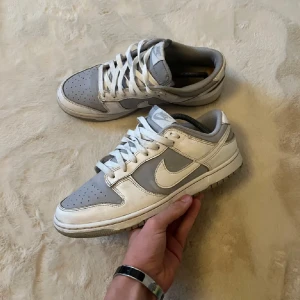 Nike Dunk Low i grått och vitt - Säljer ett par Nike Dunk Low sneakers i grått och vitt. Skorna har klassisk låg siluett, vit swoosh och snörning. Perfekta för dig som gillar stilrena och tidlösa sneakers med streetkänsla.