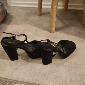 Svarta klackskor från NLY Shoes - Snygga svarta klackskor från NLY Shoes med öppen tå och justerbara remmar. Perfekta för en kväll ute eller en speciell tillställning. Klacken är stabil och ger bra stöd. Finskor med klack, mockaimitation, strl 38. Viss slitage finns, se bilder. Märke: NLY shoes.