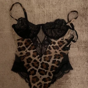 Intimissimi body - Snygg leopardmönstrad body med svarta spetsdetaljer. Den har justerbara axelband och en djup v-ringning med spets. Perfekt för en djärv look.