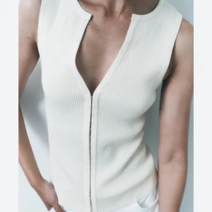 Vit ribbad linnetopp - Snygg vit ribbad linnetopp med djup v-ringning och dragkedja framtill. Perfekt för en stilren look. Intressekoll