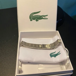 Lacoste Armband Silver  - Snyggt silverfärgat armband från Lacoste med ett stilrent och modernt mönster. Armbandet kommer i en elegant förpackning med den ikoniska krokodilloggan. Perfekt för att ge din stil en extra touch. I nyskick 💯👍