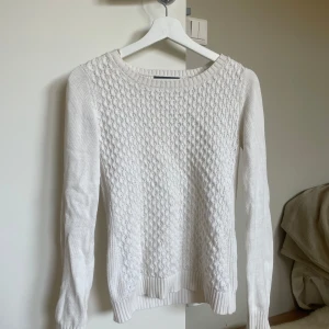 Vit stickad tröja från - Har ett litet hål vid armhålan i bak (bild 2) och en blå fläck vid ena ärmmudden (bild 4), annars inga defekter!