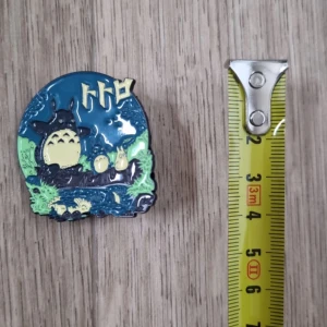 Totoro emaljpin - Säljer en färgglad emaljpin med Totoro-motiv. Pinnen har en rund form med blå, grön och gul färg. Perfekt som accessoar för att ge en personlig touch till din outfit.