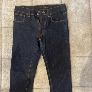 Mörkblå jeans från Nudie Jeans - Snygga mörkblå jeans från Nudie Jeans med klassisk femficksdesign och kontrasterande sömmar. Perfekta för en stilren look. OBS DOM HAR KRYMP REJÄLT MYCKET SÅ DOM ÄR STL 15/17 ish