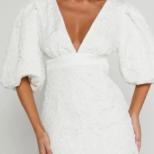 Klänning Showpo - Helt ny vit klänning från Showpo med v-ringning, framhäver midjan. Klänningen har en vacker textur och en dragkedja i ryggen. Perfekt för studenten och andra tillfällen i sommar! (Lite för kort för mig som är ganska lång därav sitter den ej perfekt på bilden på just mig) 🩷