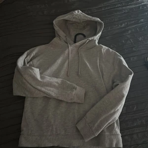 Grå hoodie från 157 - Säljer en enkel och stilren grå hoodie från 157. Tröjan har huva med dragsko och långa ärmar med ribbade muddar. Perfekt för en avslappnad look.