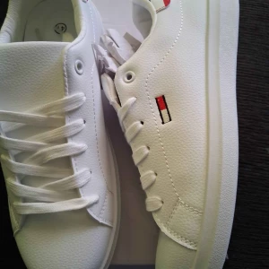 tommy hilfiger  - Snygga vita sneakers – Helt nya, storlek 41! Perfekta vardags‑ och fritidsskor för dig som vill ha en stilren look. 	•	Storlek: 41 	•	Skick: Helt oanvända, fortfarande i originalförpackning 	•	Färg: Kritvit med diskret färgad logga vid sidan 	•	Passar till: Jeans, chinos eller sommar‑shorts – ett självklart val året runt