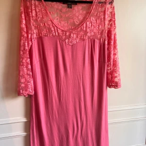 Rosa klänning med spetsdetaljer från JSFN - Säljer en söt rosa klänning från JSFN med vackra spetsdetaljer upptill och på ärmarna. Klänningen har trekvartsärmar och en rund halsringning. Perfekt för en somrig look! 🌸