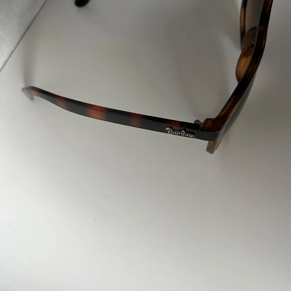 Snygga solglasögon från Ray-Ban med en klassisk brun sköldpaddsmönstrad båge. Tillverkade i Italien och har en tidlös design som passar perfekt för soliga dagar. De har mörka linser som ger ett bra skydd mot solen.. Asusteet.