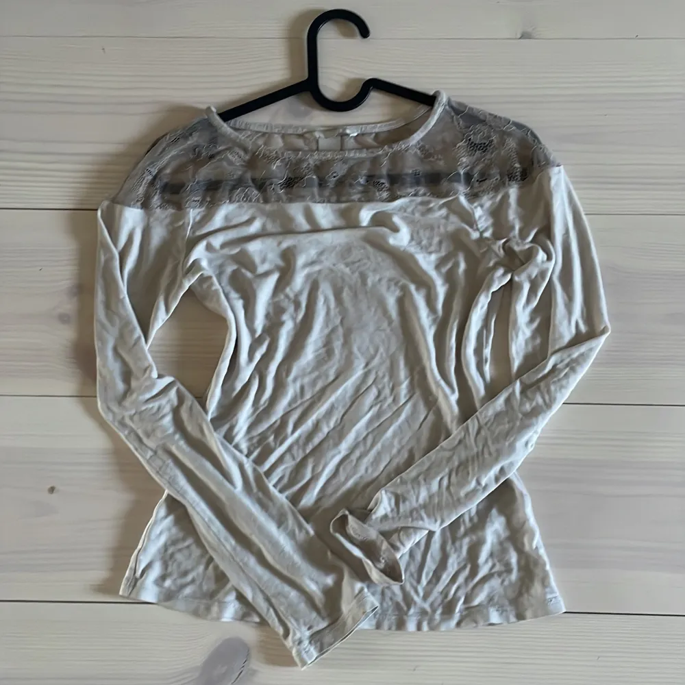 Säljer en vit långärmad topp med transparent spets upptill över axlar och bröst. Den har ett mini hål i ryggen . Neuletakit & Villapaidat.