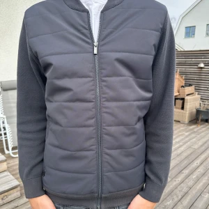 Mörkgrå cardigan från Massimo Dutti - Snygg mörkgrå cardigan från Massimo Dutti med quiltad framsida och dragkedja. Jackan har ribbade muddar och krage samt långärmade ärmar. Perfekt för en stilren look. Modellen är 193cm 82kg. Hör av er vid eventuella funderingar!