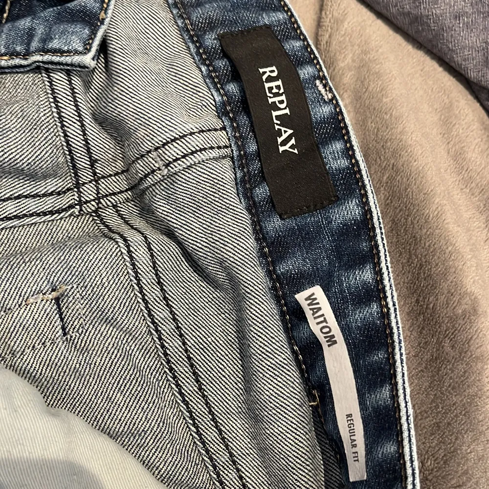 Säljer ett par blå Replay Waitom jeans med regular fit. Klassisk femficksmodell med slitningar och snygg tvätt. Skinnpatch med Replay-logga bak i midjan. Perfekta för dig som gillar en tidlös jeansstil.. Farkut & Housut.