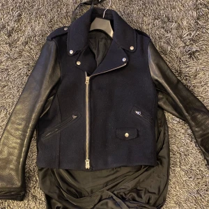 Svart bikerjacka från Acne Studios stor50 - Säljer en svart bikerjacka från Acne Studios med ullig kropp och ärmar i skinn. Jackan har silvriga dragkedjor, klassisk krage och flera fickor framtill. Snygg och stilren modell som ger en cool look.