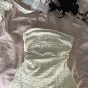 Vit axelbandslös klänning - Säljer en vit axelbandslös klänning med strukturerat tyg och figurnära passform. Perfekt för dig som vill ha en enkel men snygg look. Klänningen har en kort längd och passar till många tillfällen.